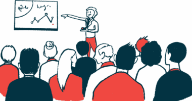 A conference presenter points to data on a white board while speaking to a large audience.