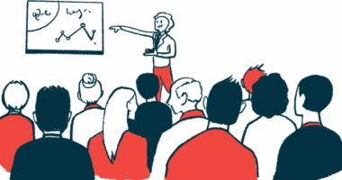 A conference presenter points to data on a white board while speaking to a large audience.