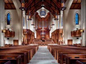 A photo depicts the empty sanctuary of a Presbyterian church, taken from the back row of pews. 