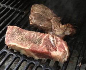 A black grill with two steaks on top. The one in the foreground is more rare.