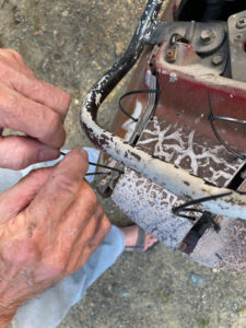 A man's hands fasten a zip tie onto the frame of an old motorcycle to help hold it together.