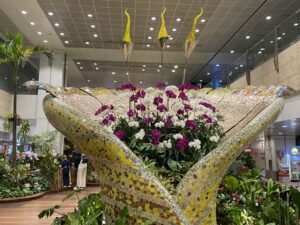 A display in what appears to be a building's lobby has red and white flowers sitting central with greenery in the opening of a yellow creation that looks something like an opening flower.