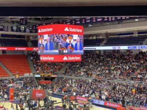 The lower levels of an indoor arena are filled with spectators, and a camera crew is set up on the court.