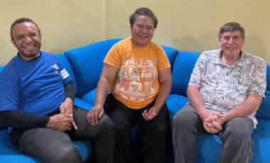 An Indonesian couple sits and visits on a blue couch with an American man.